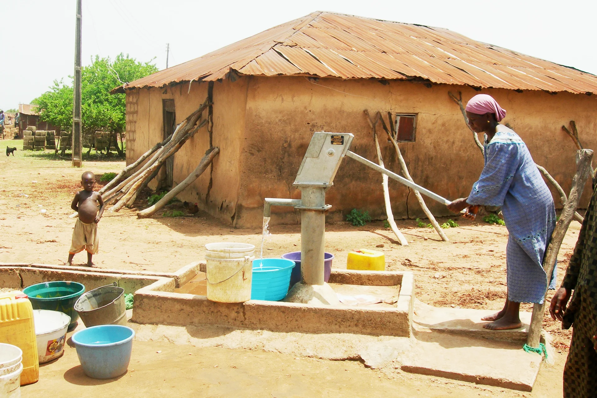 A woman operating a community handpump, with water flowing into a container